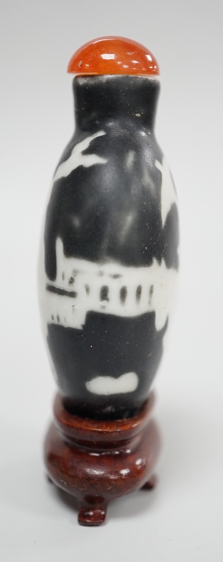 A Chinese porcelain white on black ground silhouette snuff bottle, 5.6 cm excluding stopper and wood stand